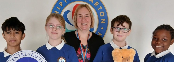 Students and a teacher have a picture taken with the IQM Award and a teddy. 